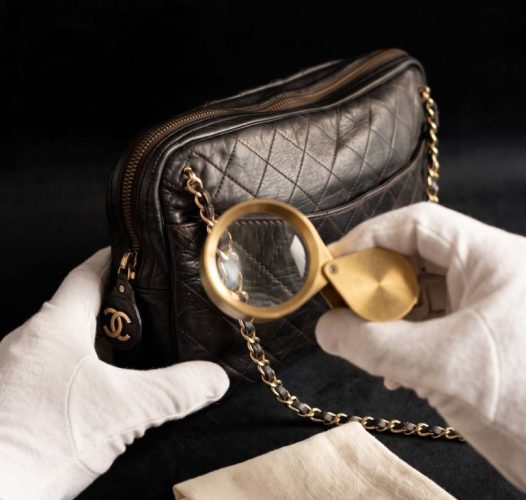 Mains gantées examinant à la loupe la piqûre sellier d'un sac de luxe, expertise à domicile en Rhône-Alpes